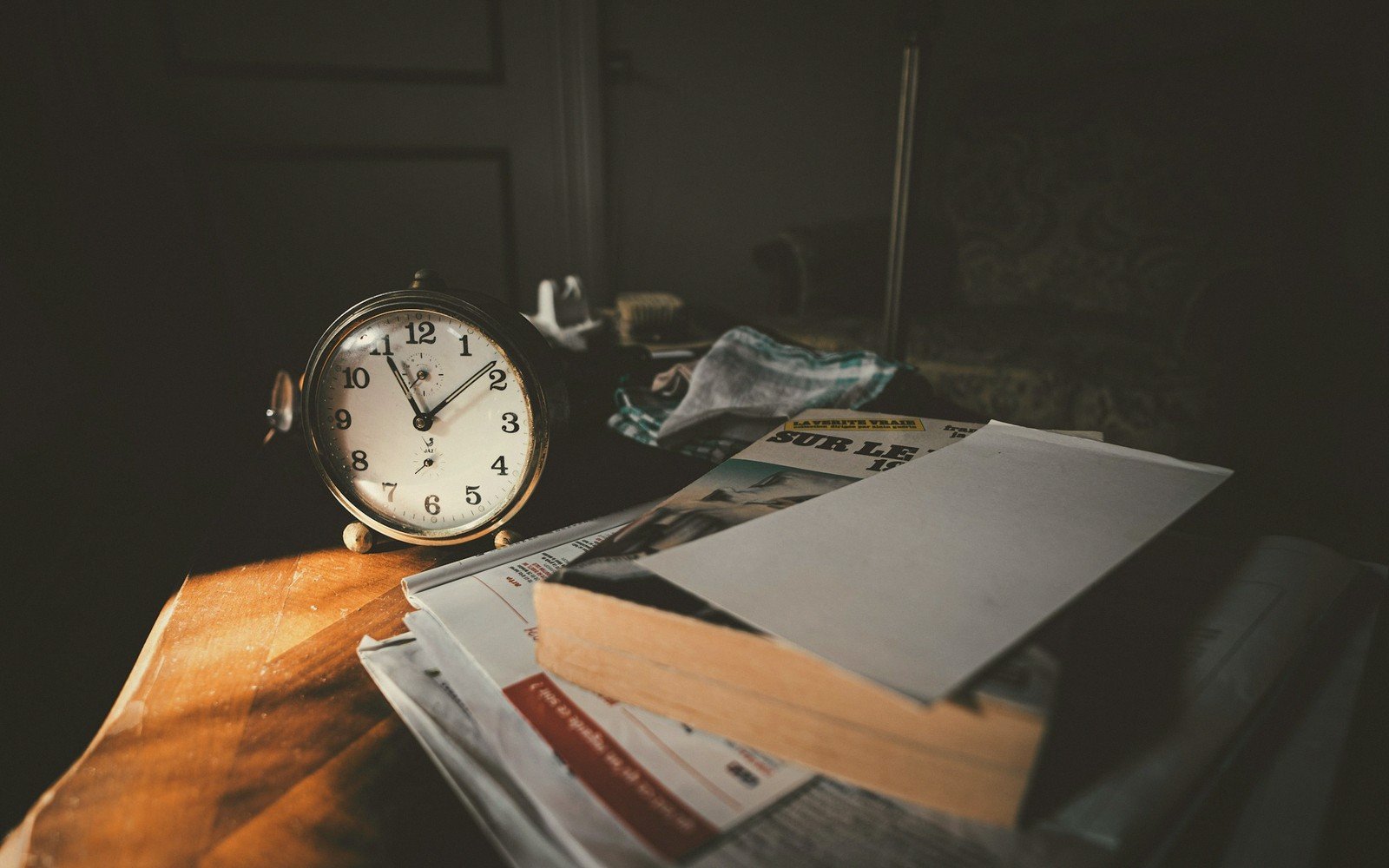 An old-fashioned alarm clock sits on a stack of newspapers and books