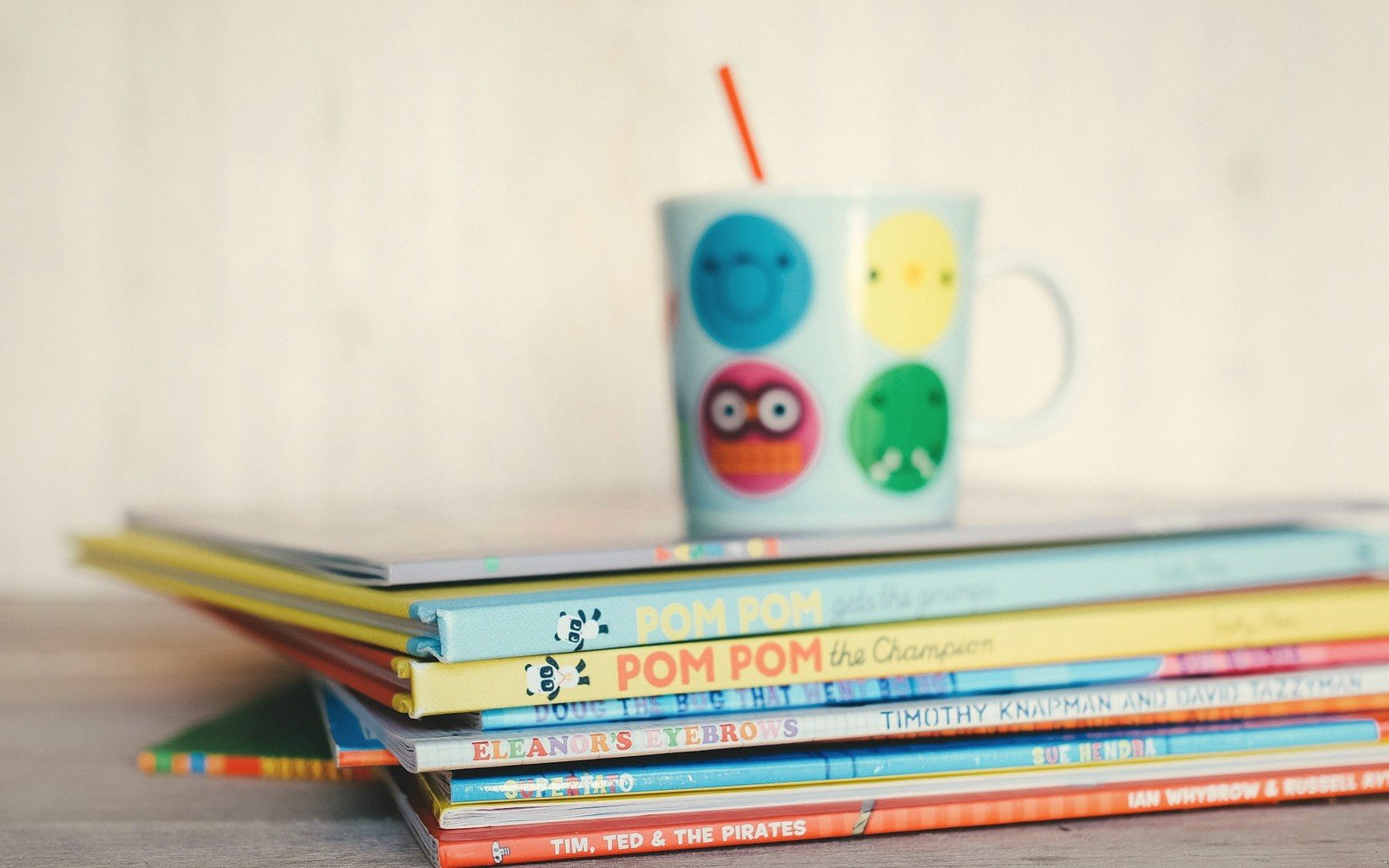 Stack of colorful children's picture books topped with a cartoon-print mug